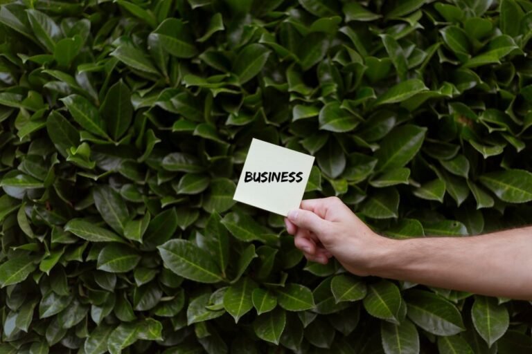 Hand holding a 'Business' note against lush green foliage. Concept of business growth in nature.