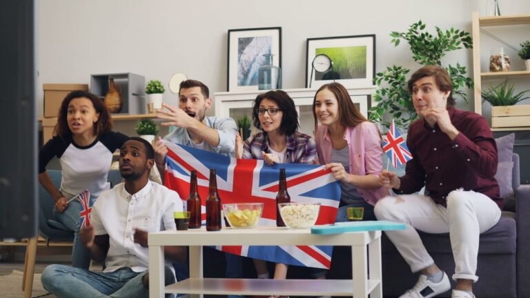 Group of friends enthusiastically watching a game at home, holding the UK flag and enjoying snacks.