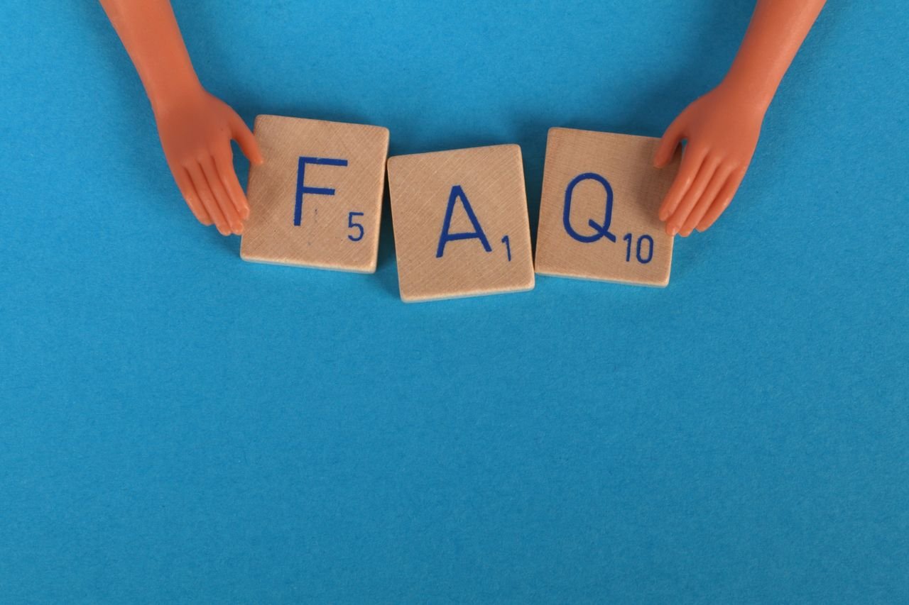 Flat lay of scrabble tiles spelling 'FAQ' with toy hands on a blue background, creating a conceptual image.