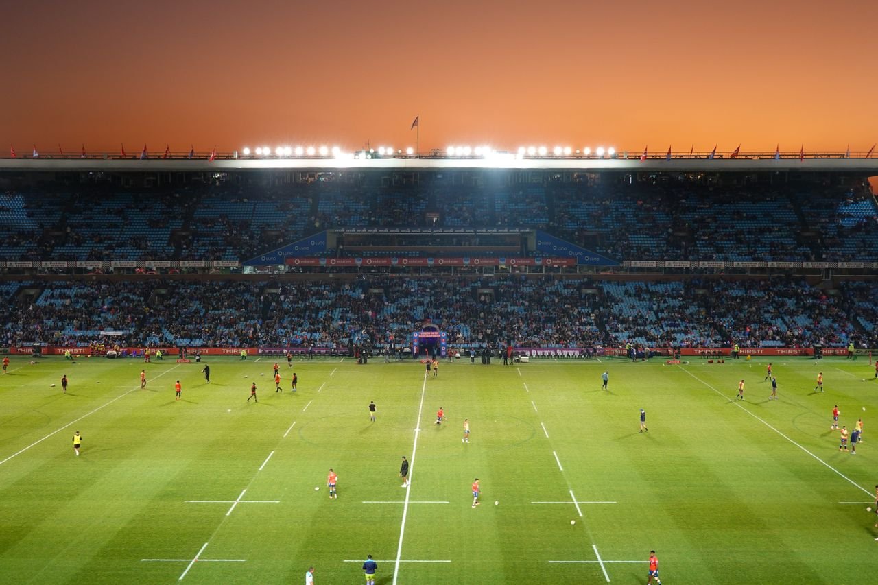 Exciting rugby game unfolding under stunning sunset in large stadium.