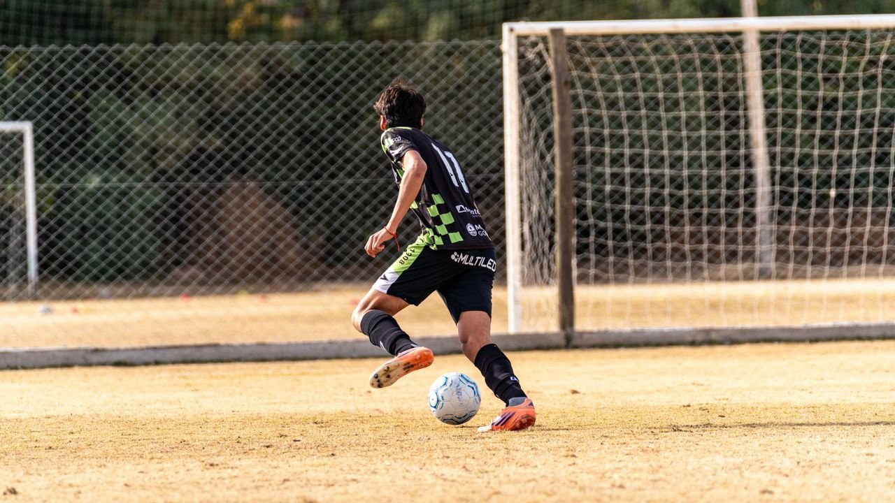 A soccer player dribbles the ball on a dry soccer field in daytime during a match.