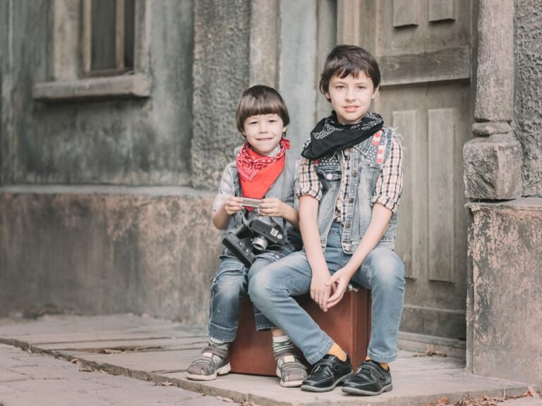 Two children sitting on a suitcase, showcasing vintage style and joy with a camera outdoors.